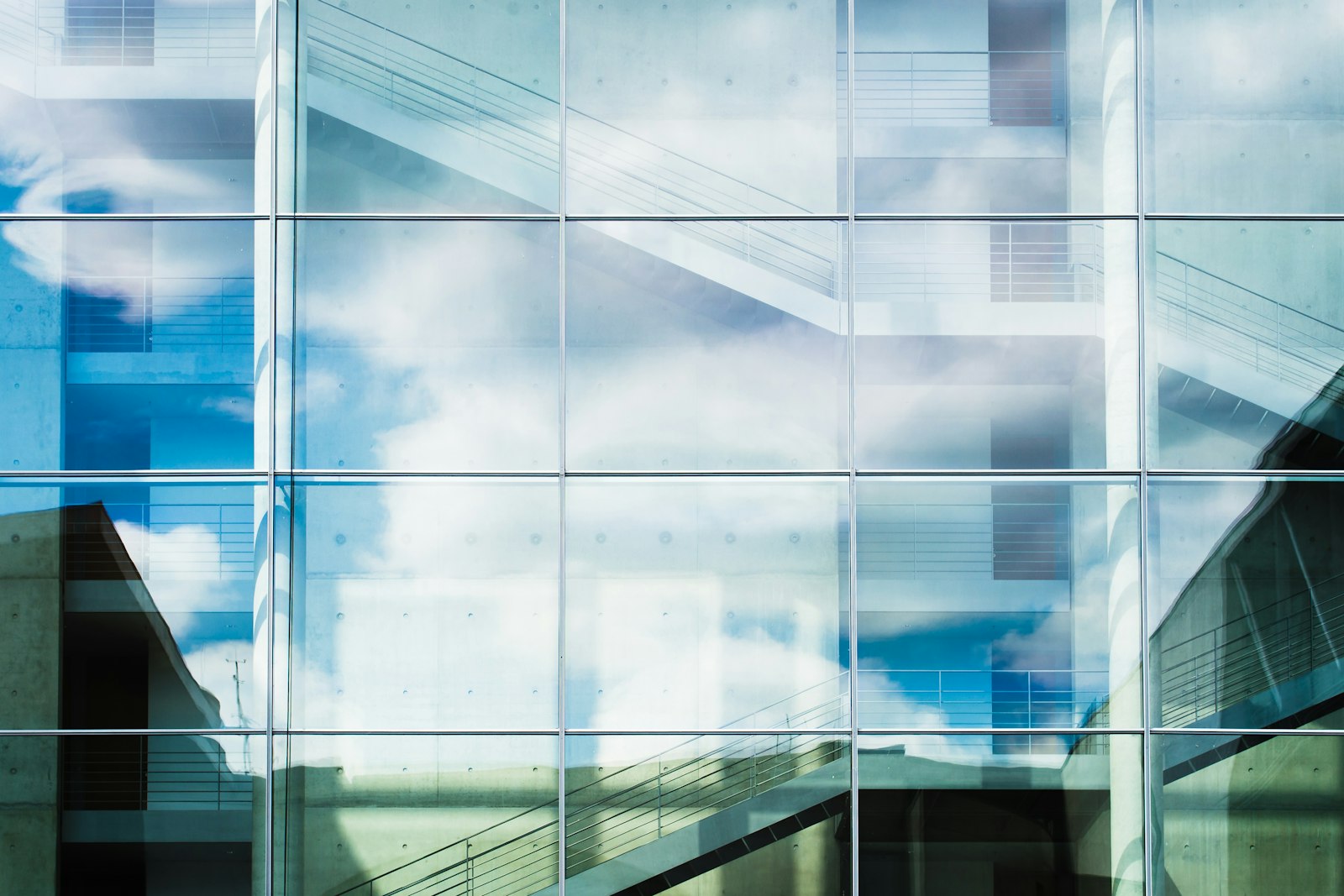 Fachada acristalada de un edificio moderno, con la retícula de montantes de aluminio y el reflejo del cielo y las nubes en los vidrios.